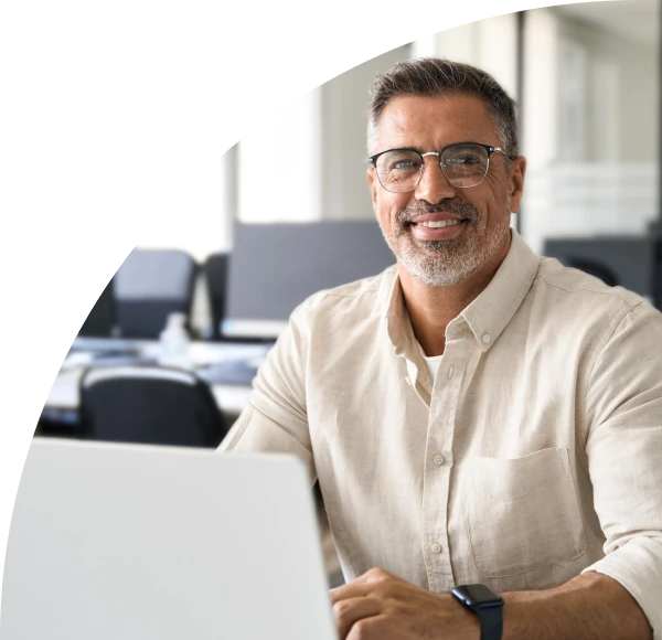 Man in business casual attire, seated behind laptop computer, smiling into camera